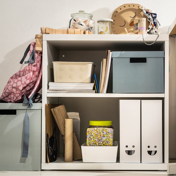 Bücherregal mit TJABBA Zeitschriftenordnern in blau und weiß, Pappkartons. Enthält Boxen, Papiere, Gläser, Holzspielzeug, Tasche.