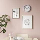 Eine stilvolle Wanduhr mit schlichtem Design. Er ist stumm, mit klaren schwarzen Ziffern auf einem weißen Zifferblatt, die darauf hinweisen, dass er mit Quarz betrieben wird.