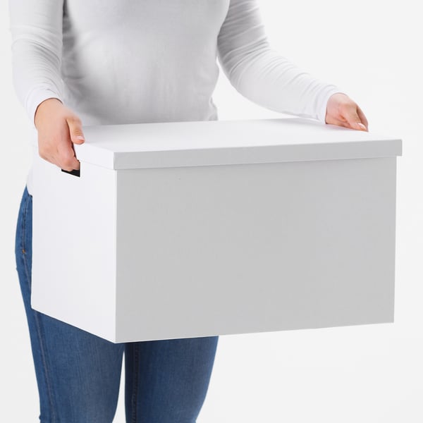 Person, die eine flache, rechteckige TJENA-Aufbewahrungsbox mit ausgeschnittenen Griffen trägt, ideal für die Aufbewahrung großer Gegenstände.