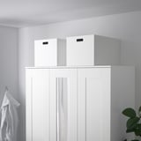 Zwei TJENA Aufbewahrungsboxen auf weißem Schrank, robust, recycelt, mit ausgeschnittenen Griffen.