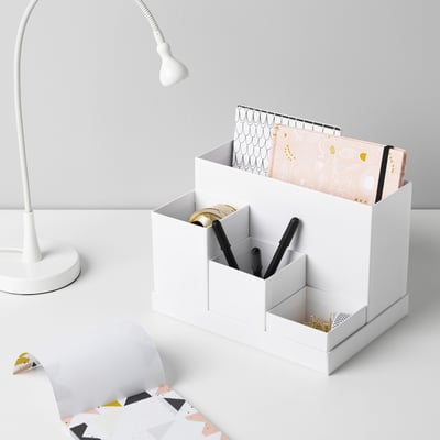 Ein weißer Schreibtisch-Organizer mit separaten Fächern für Stifte, Notizbücher und andere kleine Gegenstände. Enthält eine Lampe und gemusterte Ordner.
