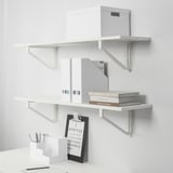 Weiße Wandregale mit Büchern, Schachteln und einem Klemmbrett mit Stiften. Organisierte Einrichtung von Home-Office-Aufbewahrung.