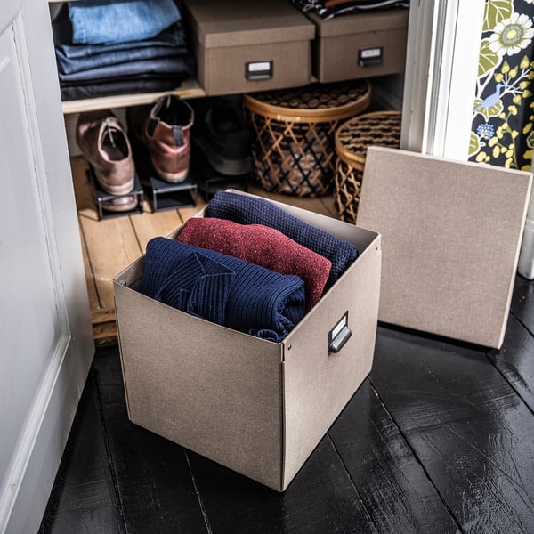 Organisierter Kleiderschrank mit gefalteter Kleidung in braunen TJOG-Boxen auf Holzboden.