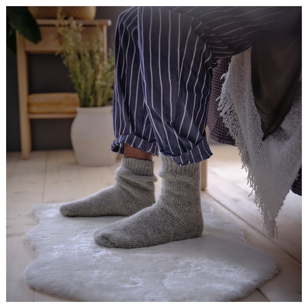 Warme Füße auf weißem TOFTLUND-Teppich, gestreifter Pyjama, gemütliches Zimmer.