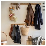 Wand mit TOLKNING-Körben, Mänteln, Handtüchern und einem Hut mit Leopardenmuster. Geflochten aus Bambus und Rattan, um einen warmen, organisierten Raum zu schaffen.