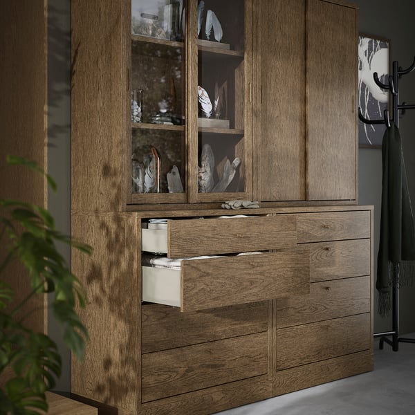 Brauner Holzschrank mit Glasschiebetüren und Schubladen, in denen Dekorationsartikel ausgestellt sind.