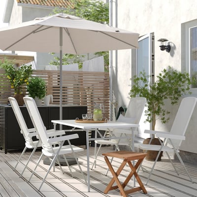 Moderne Außenterrasse mit weißen TORPARÖ-Möbeln; Großer beiger Sonnenschirm, Holzterrasse, Topfpflanzen und ein großes Glas Limonade.