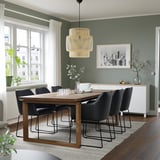 Sechs TOSSBERG-Stühle mit schwarzen Lederkissen um einen großen Esstisch aus Holz. Moderne Lampe oben, grüne Wände, Fenster draußen.