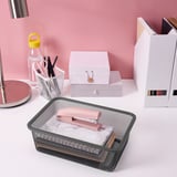 Organisierter Schreibtisch mit Aufbewahrungsbox aus Metallgitter, rosa Schere und einer weißen Box für Schreibwaren.