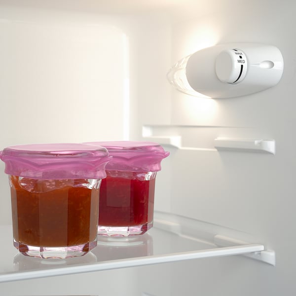 Zwei Gläser mit rosa Deckel im Kühlschrank. Gläser fassen Flüssigkeit, ein bernsteinfarbenes, ein rotes.