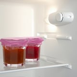 Zwei Gläser mit rosa Deckel im Kühlschrank. Gläser fassen Flüssigkeit, ein bernsteinfarbenes, ein rotes.