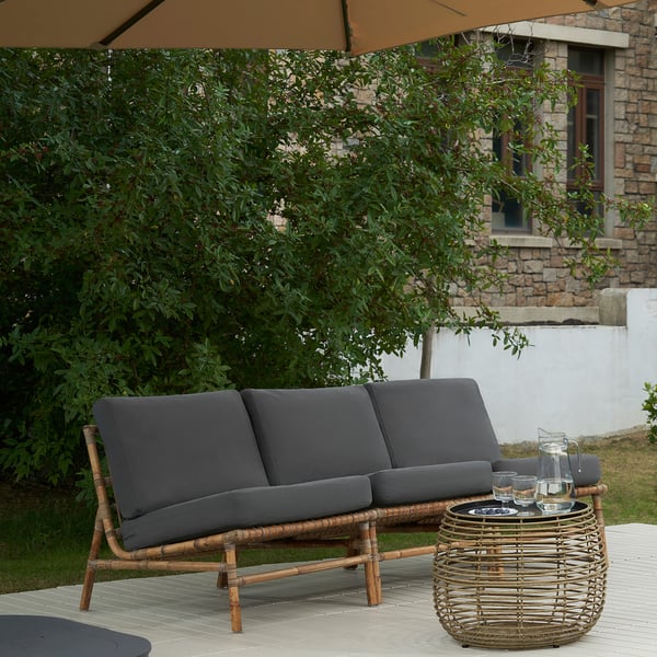 Graues TVARÖ-Sofa an Deck mit Tisch und Laub.