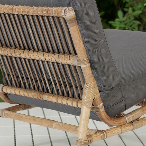 Nahaufnahme eines handgeflochtenen Outdoor-Sofas, das komplizierte Rattan-Handwerkskunst und langlebige Kissen zeigt, draußen auf einer gefliesten Terrasse.