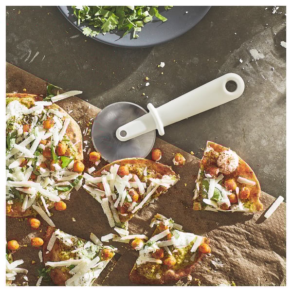 Pizzaschneider mit weißem Griff und rostfreier Klinge auf Holzbrett.