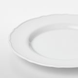 Weißer Porzellanteller mit zartem, gekräuseltem Rand, makellos und glatt, präsentiert auf einer schlichten weißen Oberfläche.