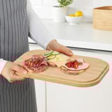 Die Person hält ein Bambustablett mit Sandwiches, Gemüse und Käse.
