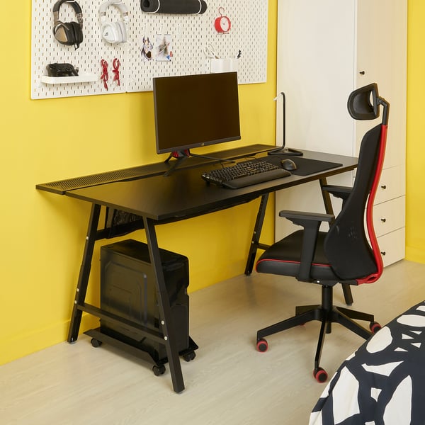 UTESPELARE Gaming-Schreibtisch in Schwarz, mittige Mittelposition, mit Monitor & Zubehör, rot-schwarzer ergonomischer Stuhl, gelber Wandhintergrund.