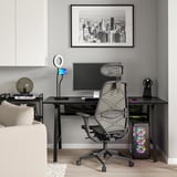 Ein modernes Home-Office-Setup mit einem schwarzen UTESPELARE-Gaming-Schreibtisch mit Netzrückenlehne, LED-Licht, Monitor und Computerturm.