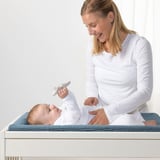 Frau wickelt Babys Windel auf VÄDRA Matte mit blau-beigem Bezug mit Katzenspielzeug.