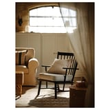 Gemütliches Wohnzimmer mit Schaukelstuhl, Sofa, Wollteppich, Korbstuhl und durchsichtigen Vorhängen.