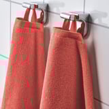 Zwei leuchtend rote Handtücher hängen ordentlich an silbernen Haken und zeigen ihre weiche, saugfähige Textur und leuchtende Farbe, ideal für den Gebrauch im Badezimmer.