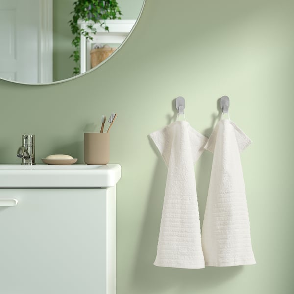 Badezimmer mit VÅGSJÖN Handtüchern an Haken, weißem Schrank und Spiegel.