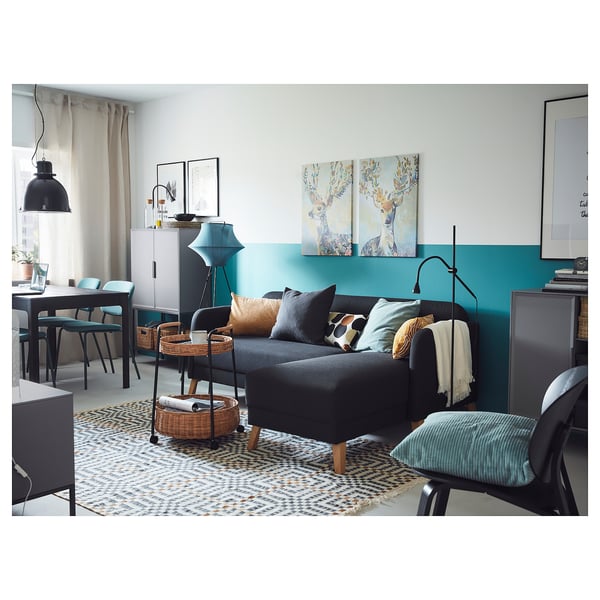 Modernes Wohnzimmer mit grauem Sofa, türkisfarbener Wand, gemustertem Teppich, schwarzen Möbeln und Kunstwerken.