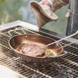Kochen in einer Pfanne aus Kohlenstoffstahl über dem Grill; Dampf steigt auf.