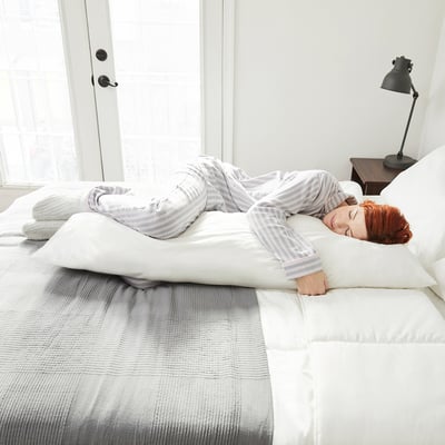 Frau ruht auf der Seite mit langem Körperkissen auf dem Bett.