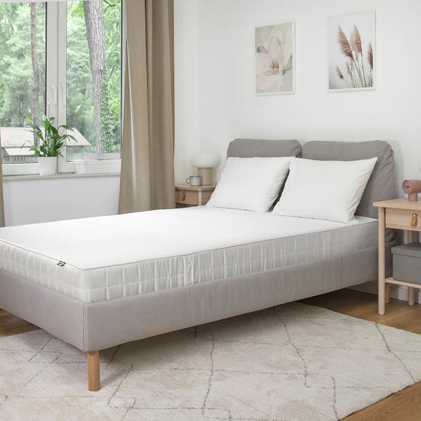 Modernes Schlafzimmer mit weißem Bett, grauem Rahmen, hellen Kissen, beigem Teppich, Vorhängen, Kunst und Holztisch.