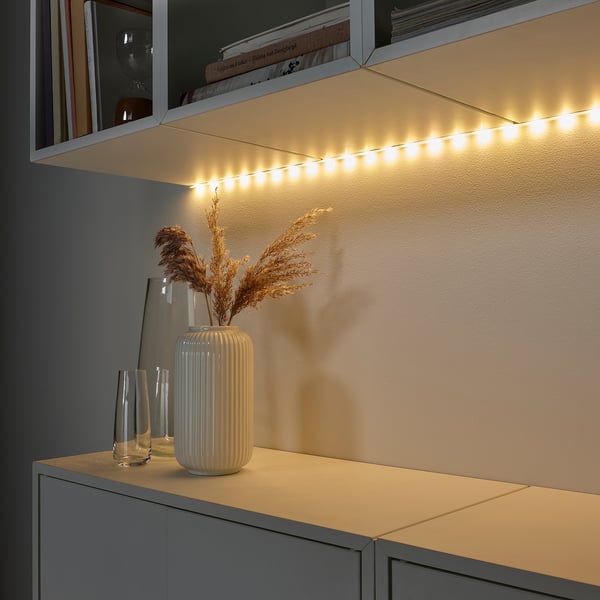 LED-Streifen beleuchten Regale mit Vasen und Pflanzen warm.