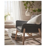 Dunkelgrauer moderner Sessel mit Holzbeinen, weichen Kissen, lichtdurchflutetem Raum, Büchern, Pflanze und Hängelampe.
