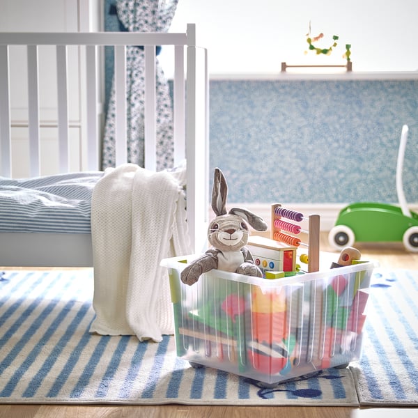 Kinderzimmer mit VESSLA-Spielzeugkiste auf blauem Teppich neben dem Kinderbett.