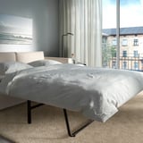 Modernes Schlafzimmer mit großem Fenster, Schlafsofa mit dicker Matratze und Stadtblick.