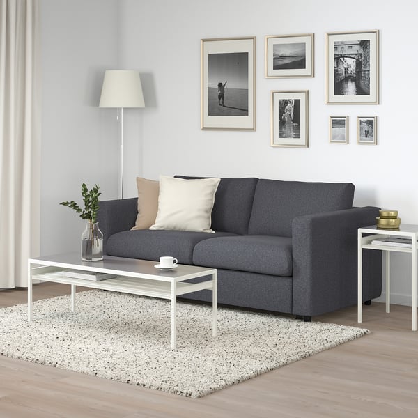 Modernes Wohnzimmer mit grauem VIMLE-Sofa, weißem Couchtisch und gerahmten Schwarz-Weiß-Fotos an weißer Wand.