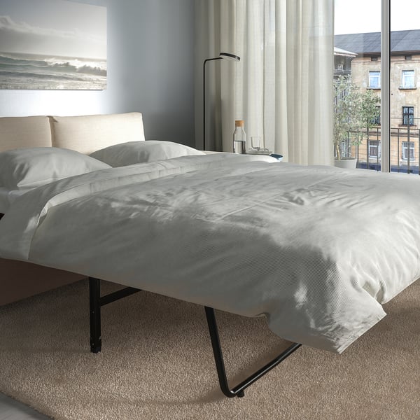 Ein modernes Schlafzimmer mit einem grauen VIMLE-Schlafsofa mit einer dicken Matratze vor einem großen Fenster mit Blick auf die Stadt, minimalistische Einrichtung.