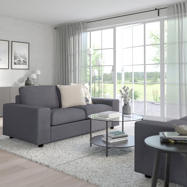 Modernes Wohnzimmer mit großem VIMLE Sofa in Grau; minimalistische Einrichtung, große Fenster mit Vorhängen.