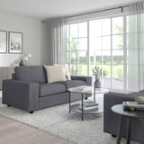 Modernes Wohnzimmer mit großem VIMLE Sofa in Grau; minimalistische Einrichtung, große Fenster mit Vorhängen.