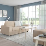 Beiges VIMLE Sofa, grauer Teppich, weißer Couchtisch, große Fenster, Lampe, Dekor.