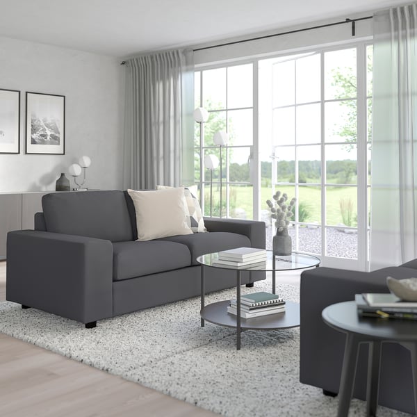 Modernes Wohnzimmer mit grauem Sofa, Couchtisch aus Glas und großen Fenstern.