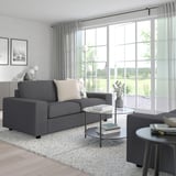 Modernes Wohnzimmer mit grauem Sofa, Couchtisch aus Glas und großen Fenstern.