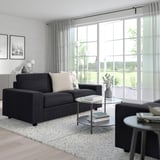 Modernes Wohnzimmer mit dunkelgrauem VIMLE-Sofa, Couchtischen aus Glas, Teppich, Lampe, Kunst und Fenster.