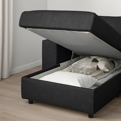Das Bild zeigt ein dunkelgraues VIMLE-Sofa mit offenem Stauraum unter dem Sitz, der Bettzeug und Kissen im Inneren freigibt.