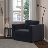 Modernes Wohnzimmer mit marineblauem VIMLE-Sessel, Lampe, Beistelltisch, grauen Vorhängen, Parkettboden und Teppich.