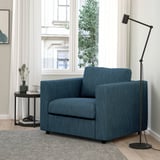 Modernes Wohnzimmer mit blauem VIMLE-Sessel, hellem Holzboden, Teppich, schwarzer Stehlampe und kleinem Tisch mit Kaffeetasse und Pflanze.