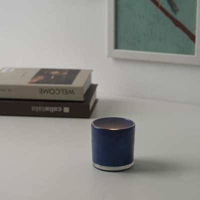 Dunkelblauer Kerzenhalter auf weißem Tisch mit Büchern.