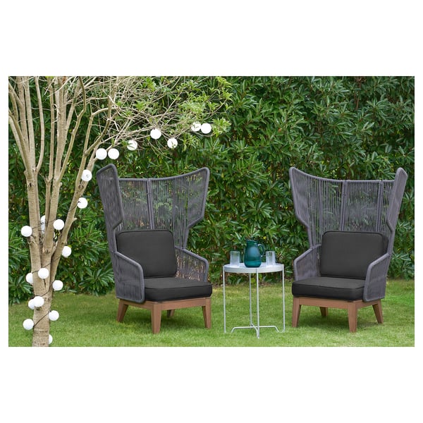 Zwei graue VINGSÖN Outdoor-Sessel mit hohen Rückenlehnen auf einer Rasenfläche, umgeben von Grün und weißem Licht.