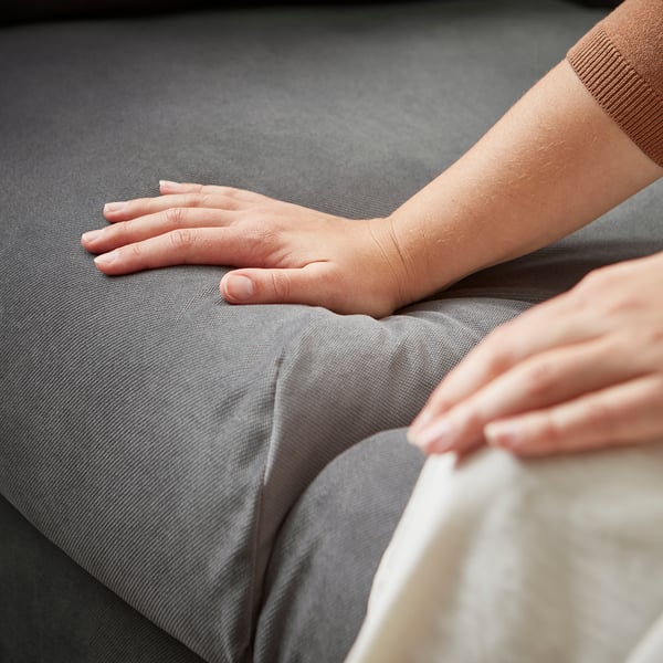 Person auf grauem VINLIDEN-Sofa mit weichen Kissen und hoher Rückenlehne, modernes, minimalistisches Design.