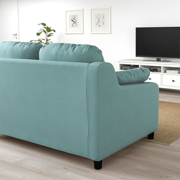 Ein hellblaues VINLIDEN-Sofa in einem Wohnzimmer, geräumig mit hohen Rückenkissen, in der Nähe eines TV-Ständers und eines Teppichs.