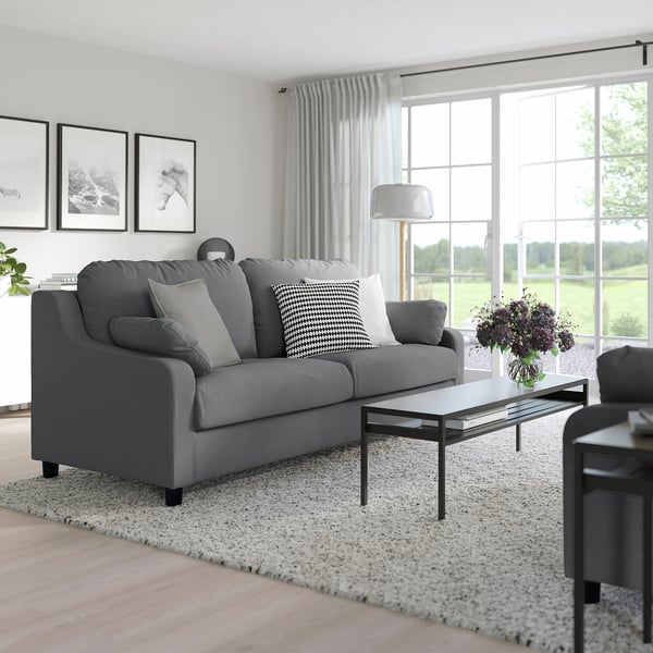 Modernes Wohnzimmer mit grauem VINLIDEN-Sofa, Kissen und Couchtisch mit Blumen.